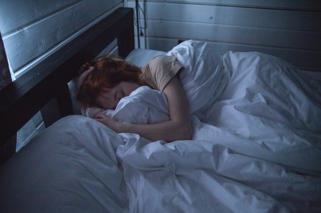 Žena ležiaca na posteli zababušená v perinách